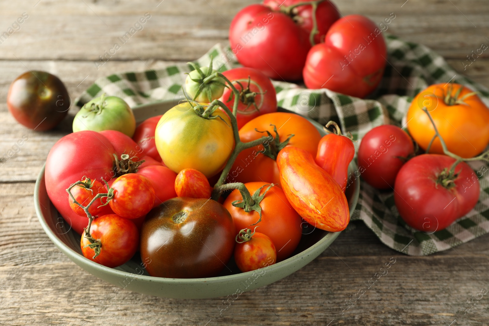 Photo of Different ripe tomatoes in bowl on wooden table