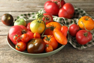 Different ripe tomatoes in bowl on wooden table