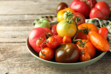 Different ripe tomatoes in bowl on wooden table, closeup