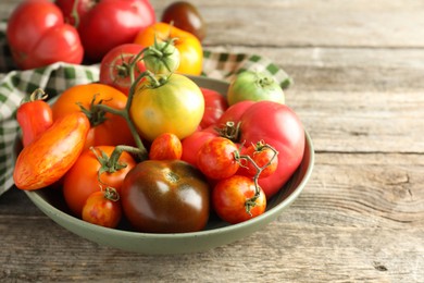 Photo of Different ripe tomatoes in bowl on wooden table, closeup