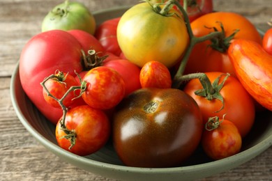 Different ripe tomatoes in bowl on wooden table, closeup