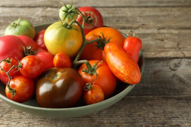 Different ripe tomatoes in bowl on wooden table, closeup