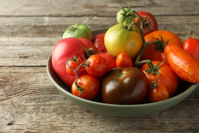 Different ripe tomatoes in bowl on wooden table, closeup