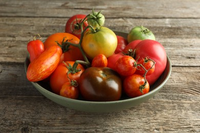 Photo of Different ripe tomatoes in bowl on wooden table