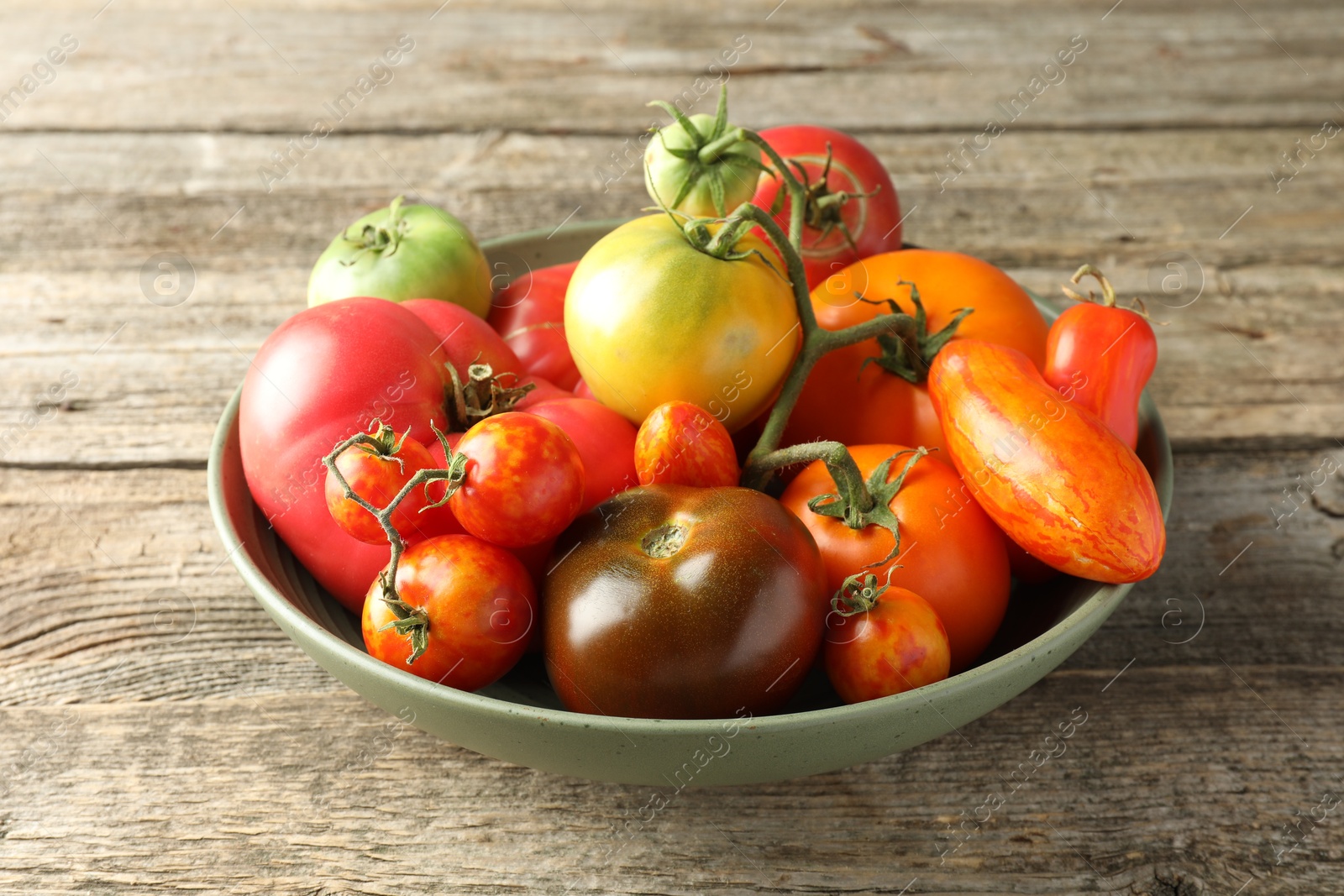 Photo of Different ripe tomatoes in bowl on wooden table