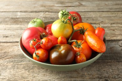 Different ripe tomatoes in bowl on wooden table