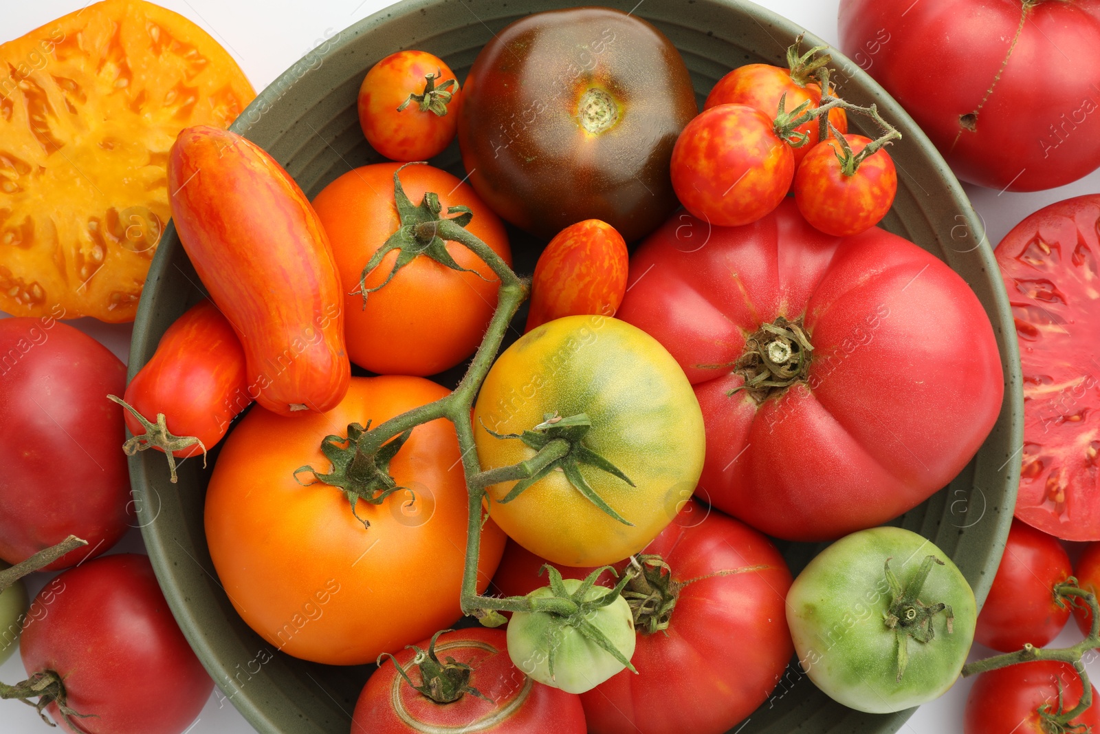 Photo of Different ripe tomatoes in bowl on white background, flat lay