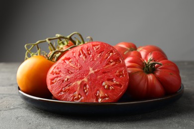 Different whole and cut ripe tomatoes on grey table, closeup