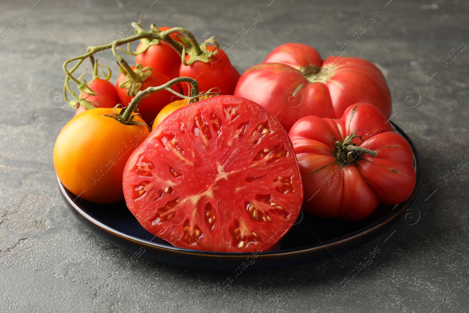 Photo of Different whole and cut ripe tomatoes on grey table, closeup