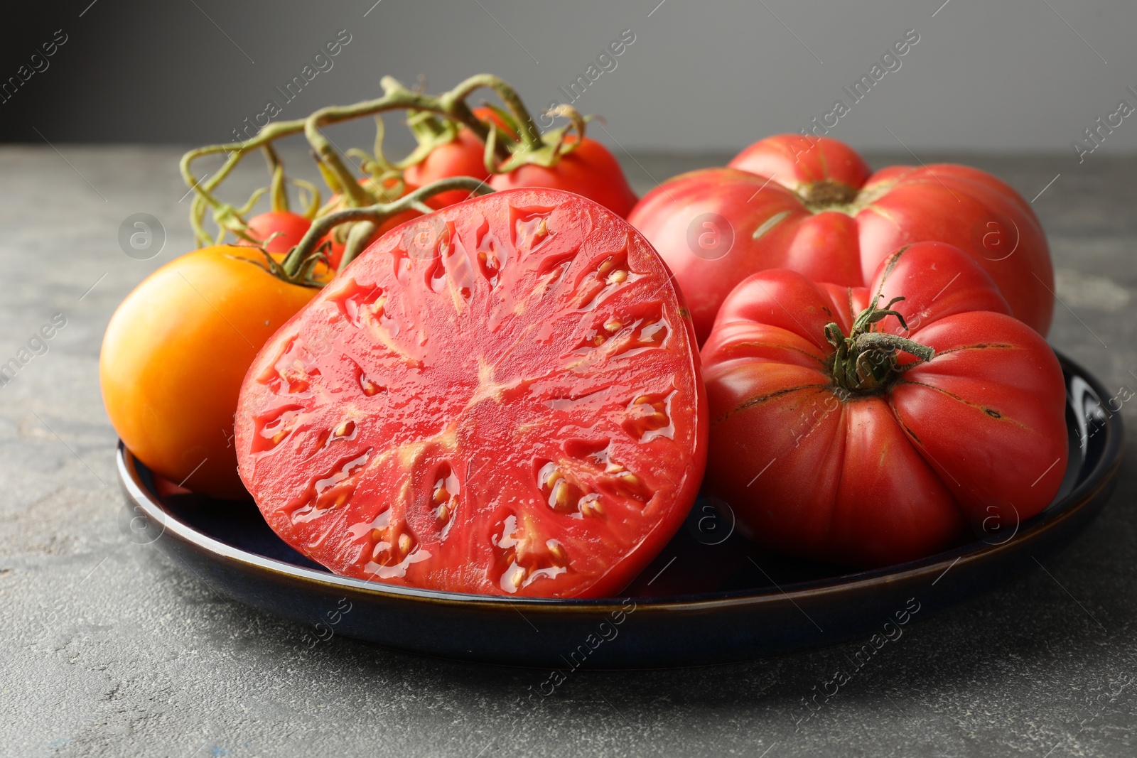 Photo of Different whole and cut ripe tomatoes on grey table, closeup