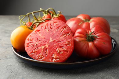 Different whole and cut ripe tomatoes on grey table, closeup