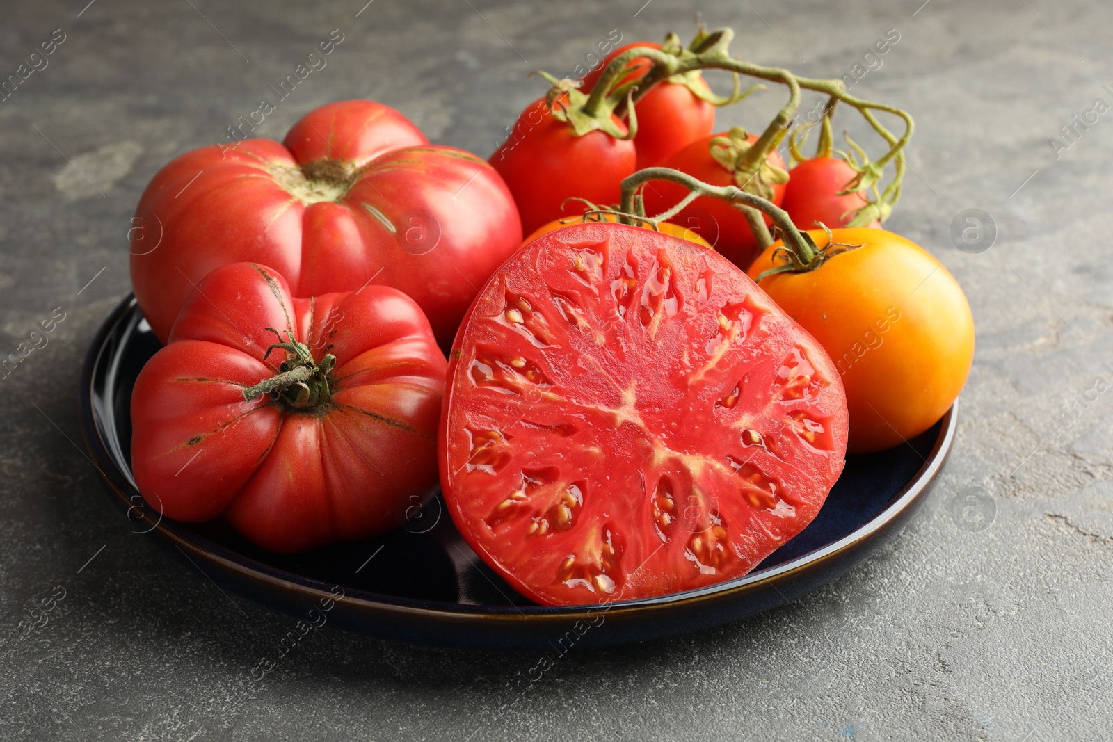 Photo of Different whole and cut ripe tomatoes on grey table, closeup