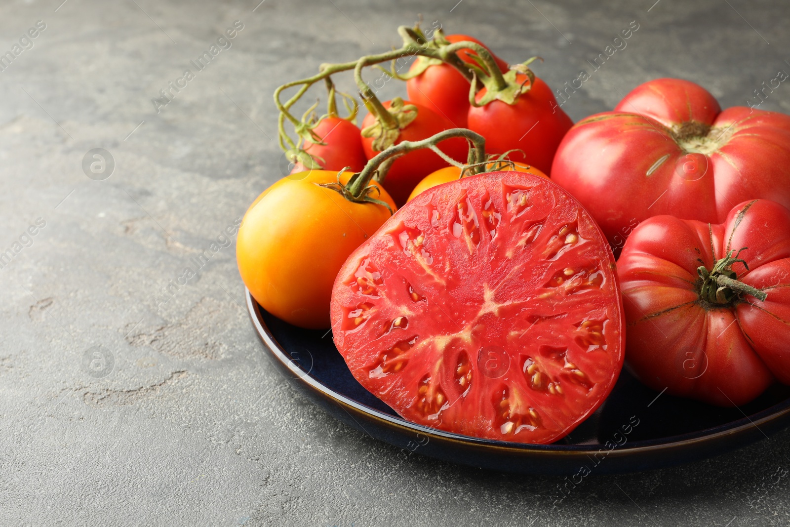 Photo of Different whole and cut ripe tomatoes on grey table, closeup