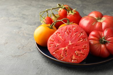 Different whole and cut ripe tomatoes on grey table, closeup