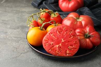 Different whole and cut ripe tomatoes on grey table