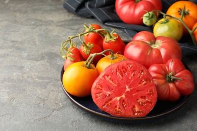 Different whole and cut ripe tomatoes on grey table