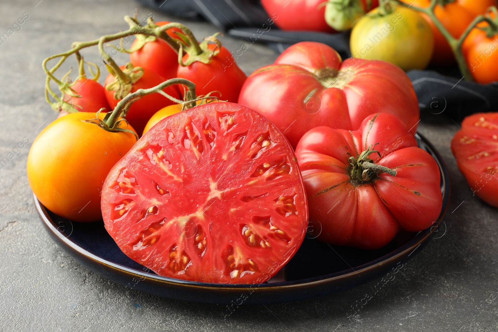 Photo of Different whole and cut ripe tomatoes on grey table, closeup