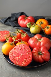 Different whole and cut ripe tomatoes on grey table