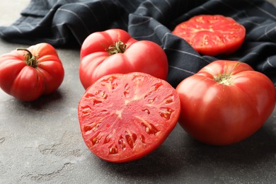 Photo of Whole and cut ripe red tomatoes on grey table, closeup