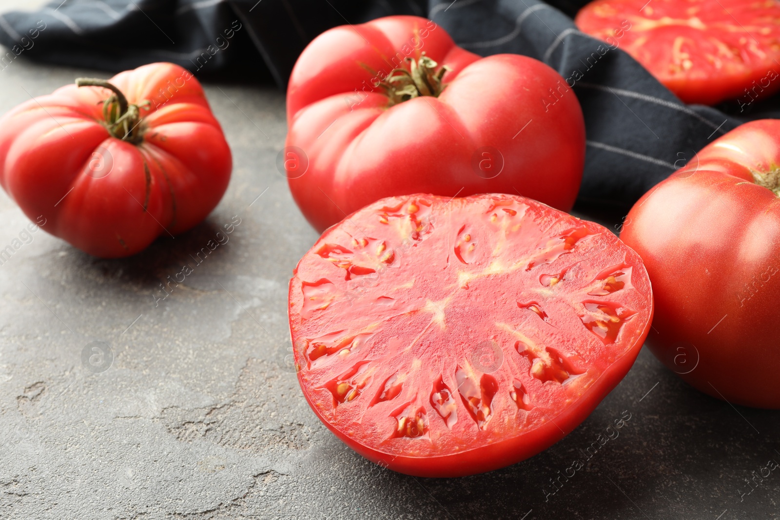 Photo of Whole and cut ripe red tomatoes on grey table, closeup