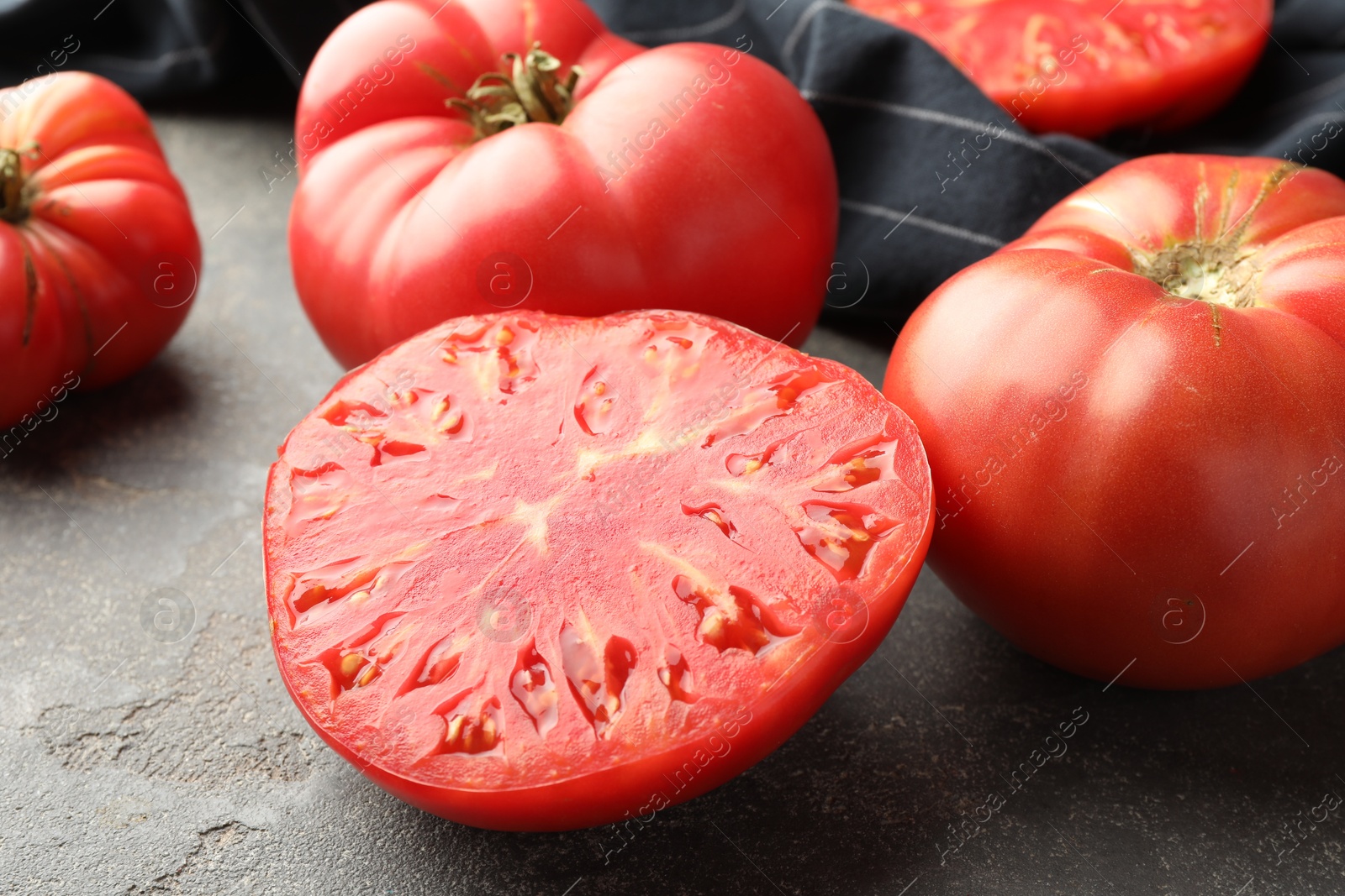 Photo of Whole and cut ripe red tomatoes on grey table, closeup