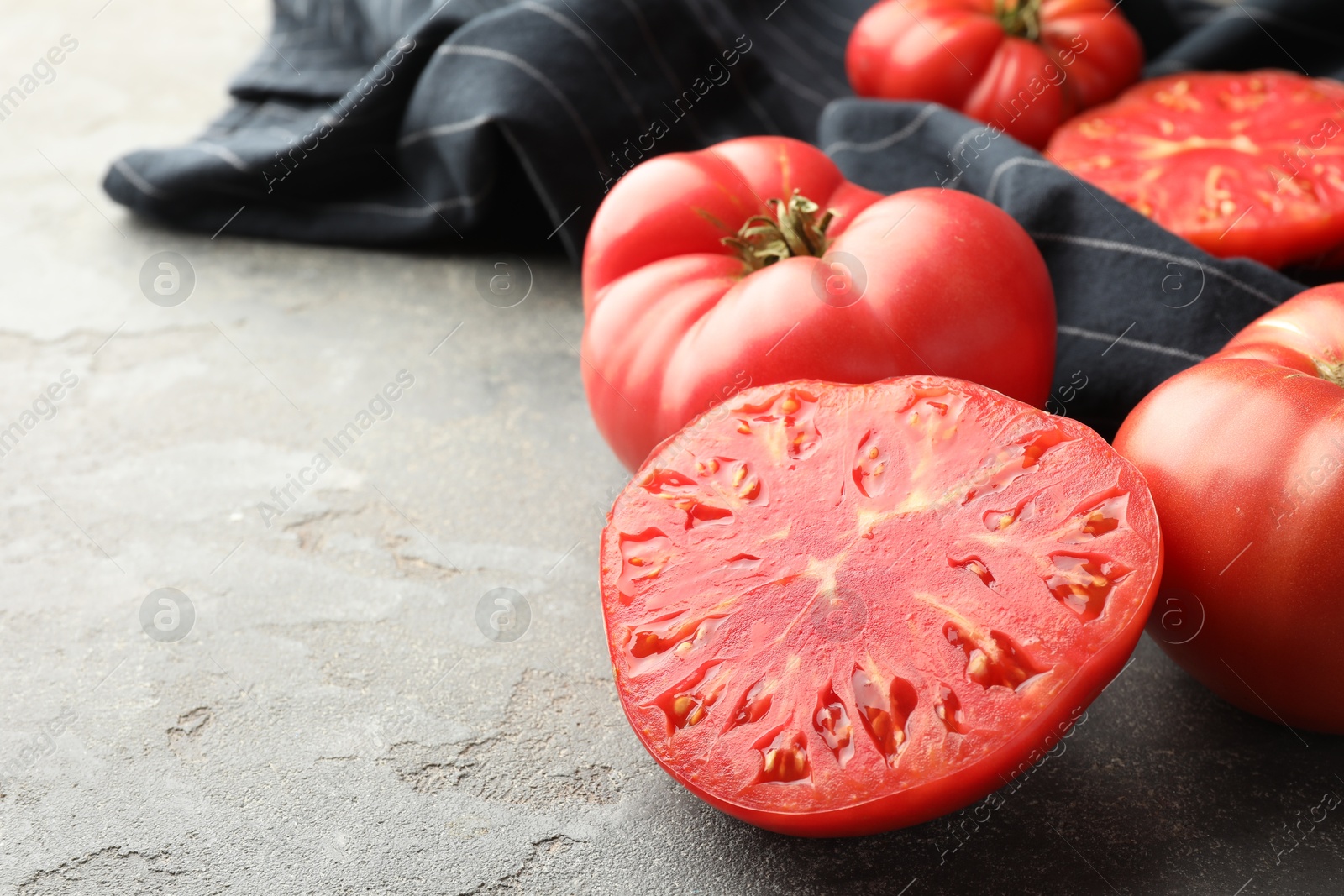 Photo of Whole and cut ripe red tomatoes on grey table, closeup. Space for text