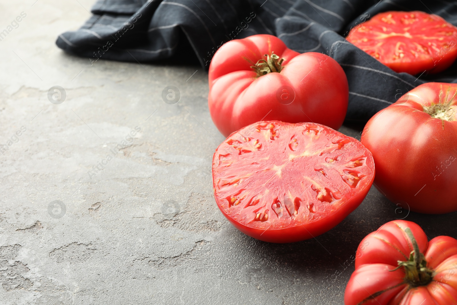 Photo of Whole and cut ripe red tomatoes on grey table, closeup. Space for text