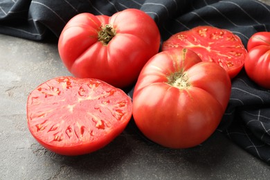 Photo of Whole and cut ripe red tomatoes on grey table, closeup