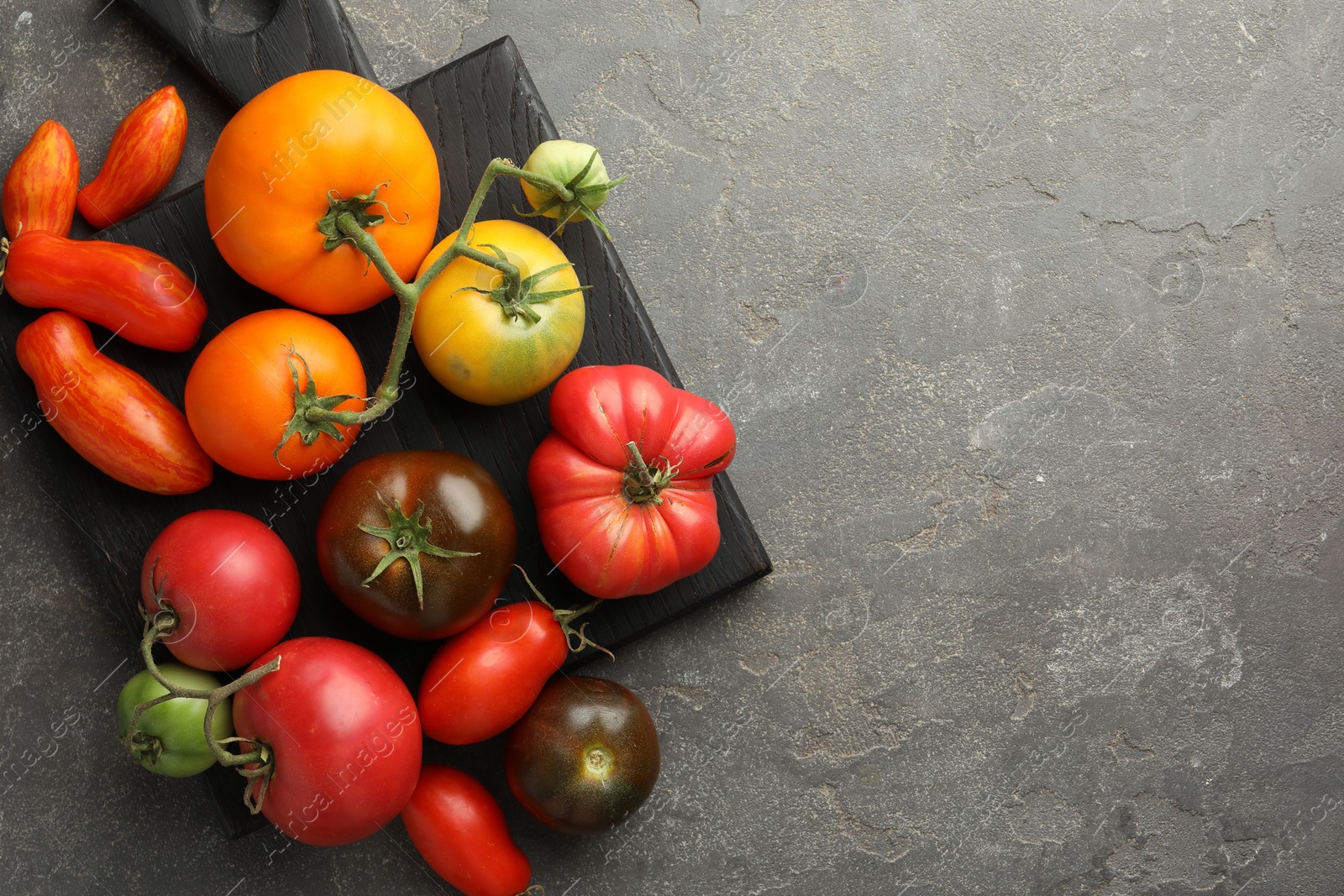 Photo of Different ripe tomatoes on grey table, top view. Space for text