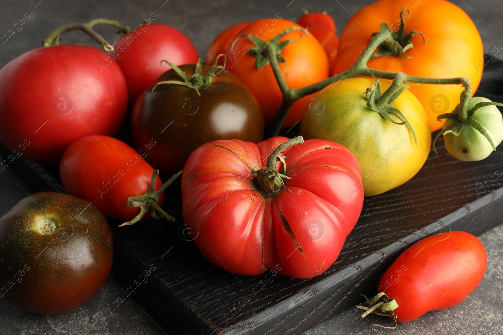 Photo of Different ripe tomatoes on grey table, closeup