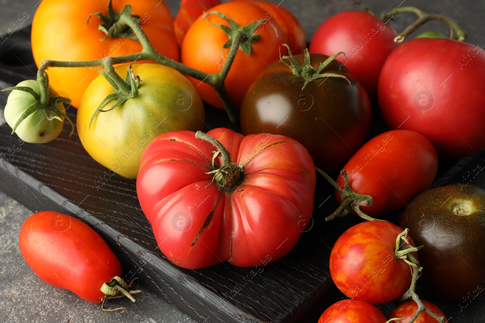 Photo of Different ripe tomatoes on grey table, closeup