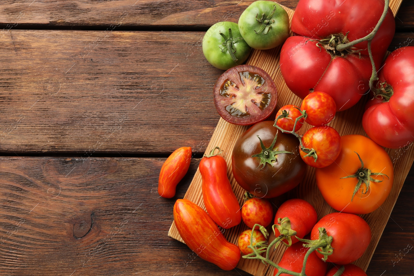 Photo of Different ripe tomatoes on wooden table, top view. Space for text