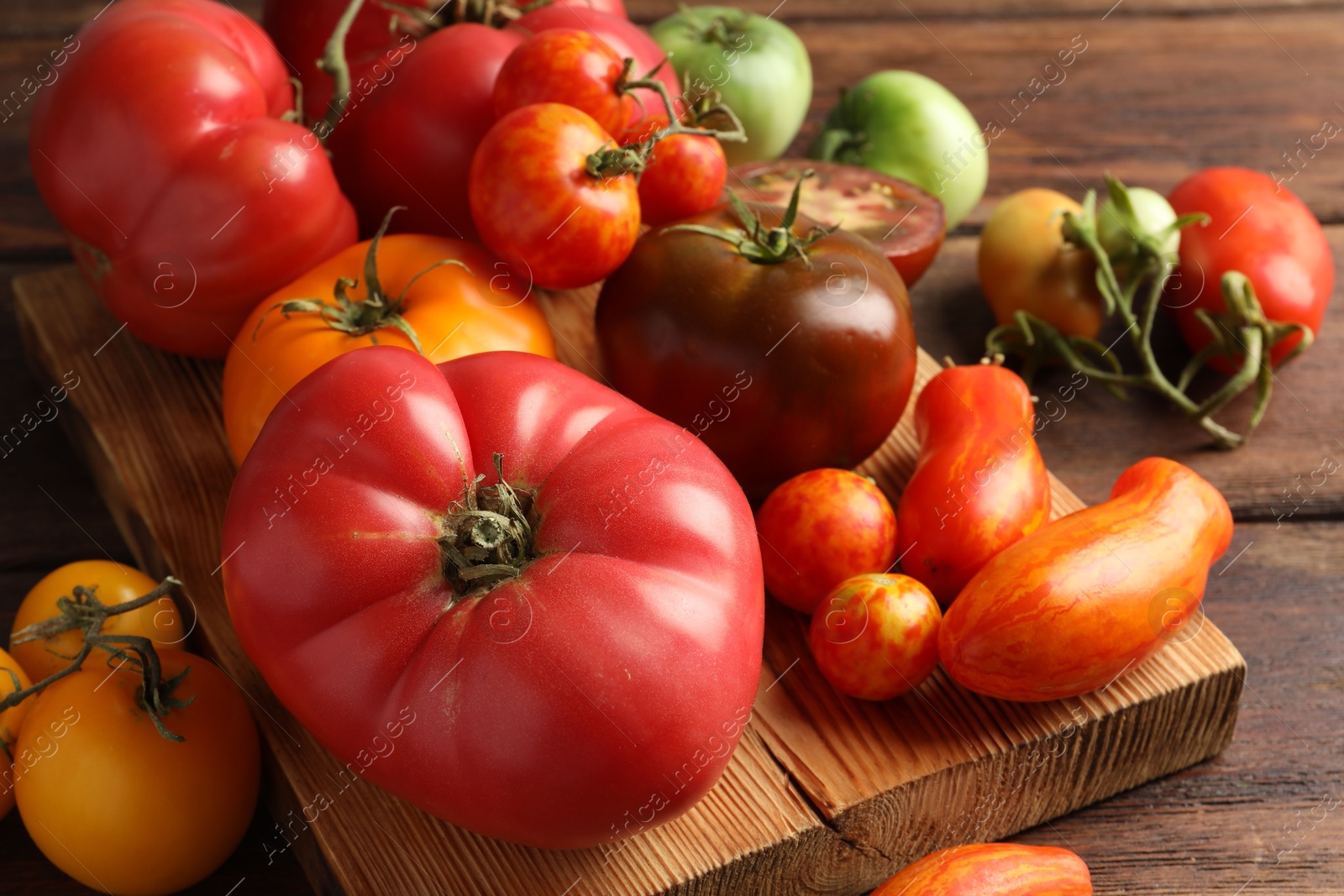 Photo of Different ripe tomatoes on wooden table, closeup