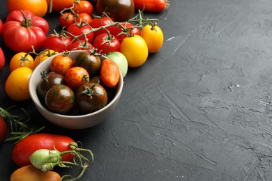 Photo of Different fresh tomatoes on grey textured table. Space for text