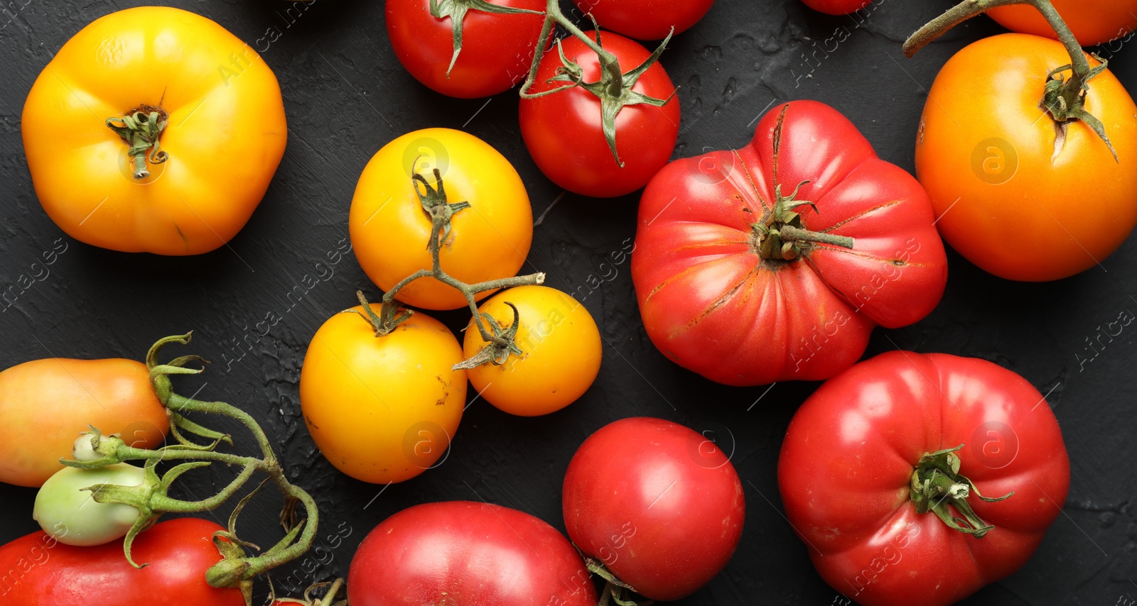 Photo of Different fresh tomatoes on grey textured table, flat lay