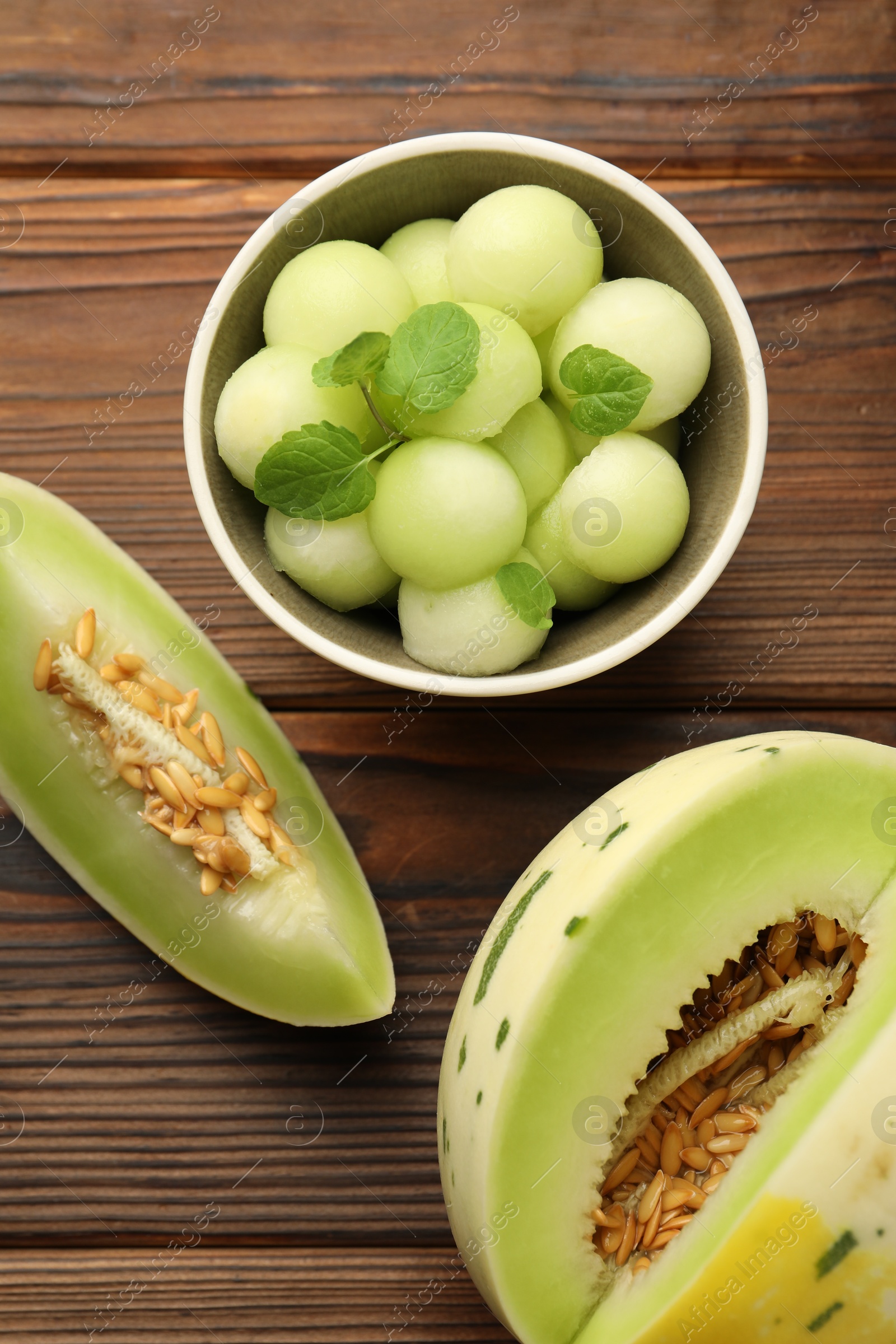 Photo of Melon balls in bowl and fresh fruit on wooden table, flat lay