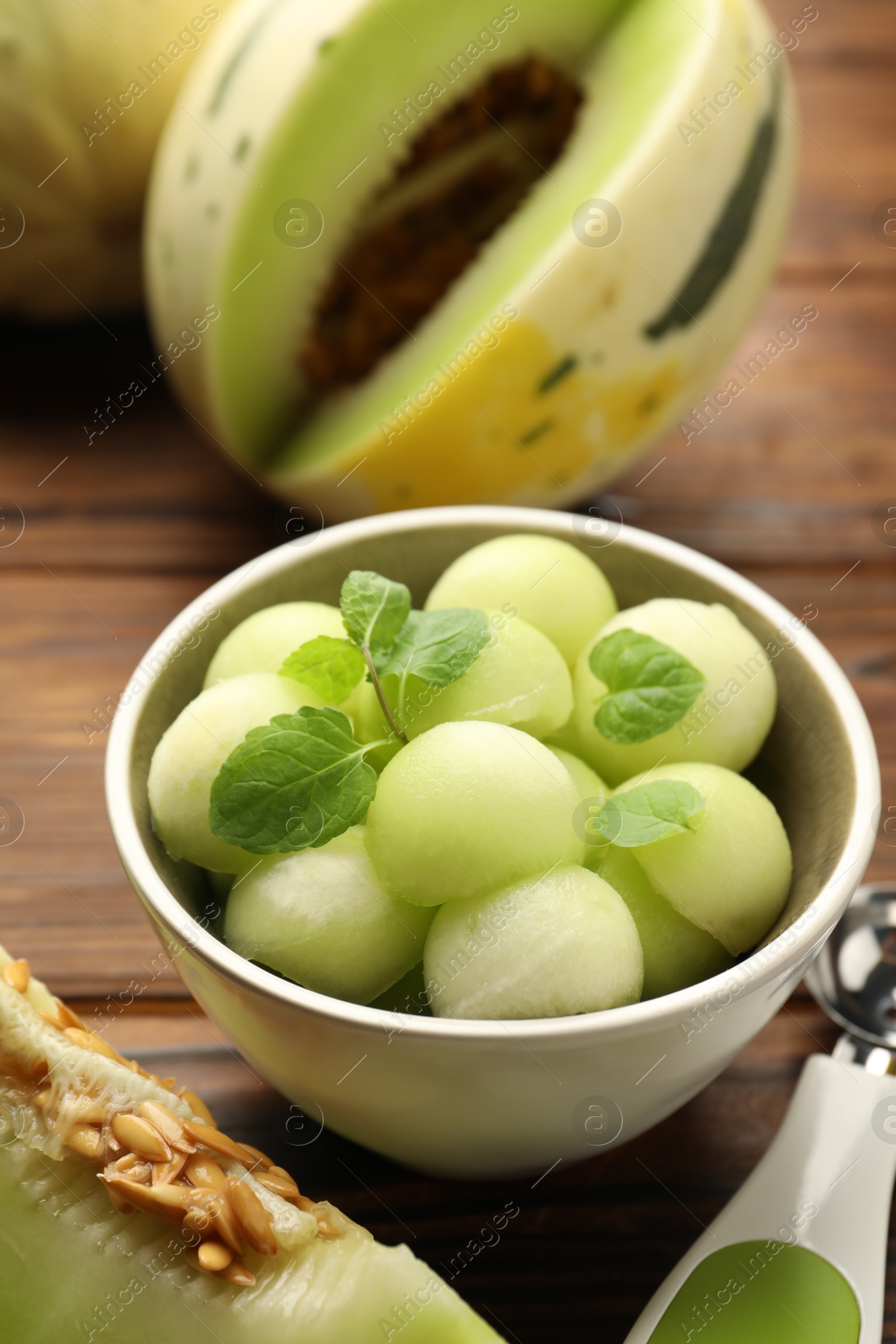 Photo of Melon balls in bowl and fresh fruit on wooden table, closeup