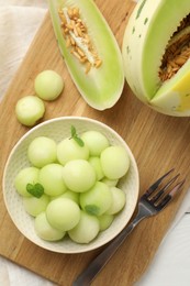 Photo of Melon balls in bowl and fresh fruit on white wooden table, top view