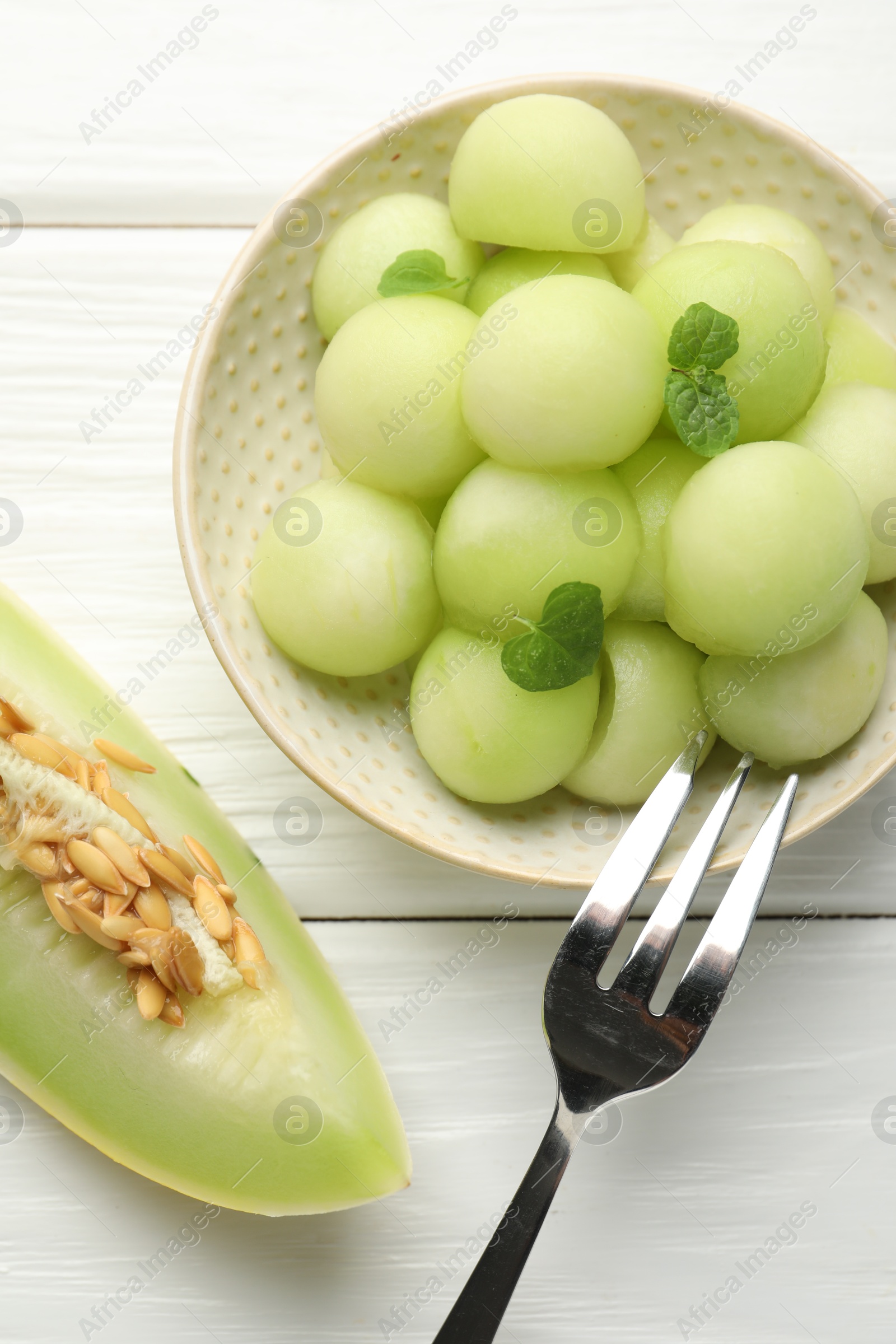 Photo of Melon balls in bowl and fresh fruit on wooden table, top view