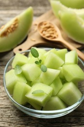 Photo of Slices of yummy melon in glass bowl on wooden table, closeup