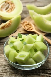 Photo of Slices of yummy melon in glass bowl on wooden table, closeup