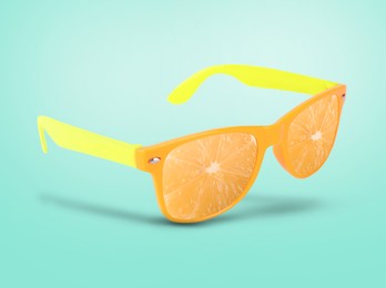 Image of Sunglasses with juicy orange in air on turquoise background. Summer vibe