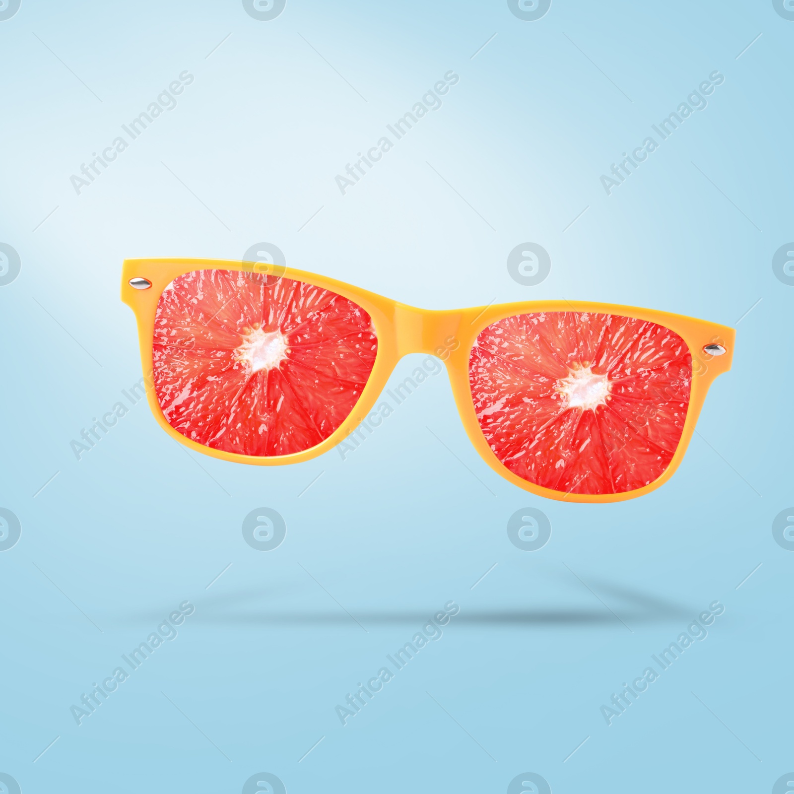 Image of Sunglasses with juicy grapefruit in air on light blue background. Summer vibe