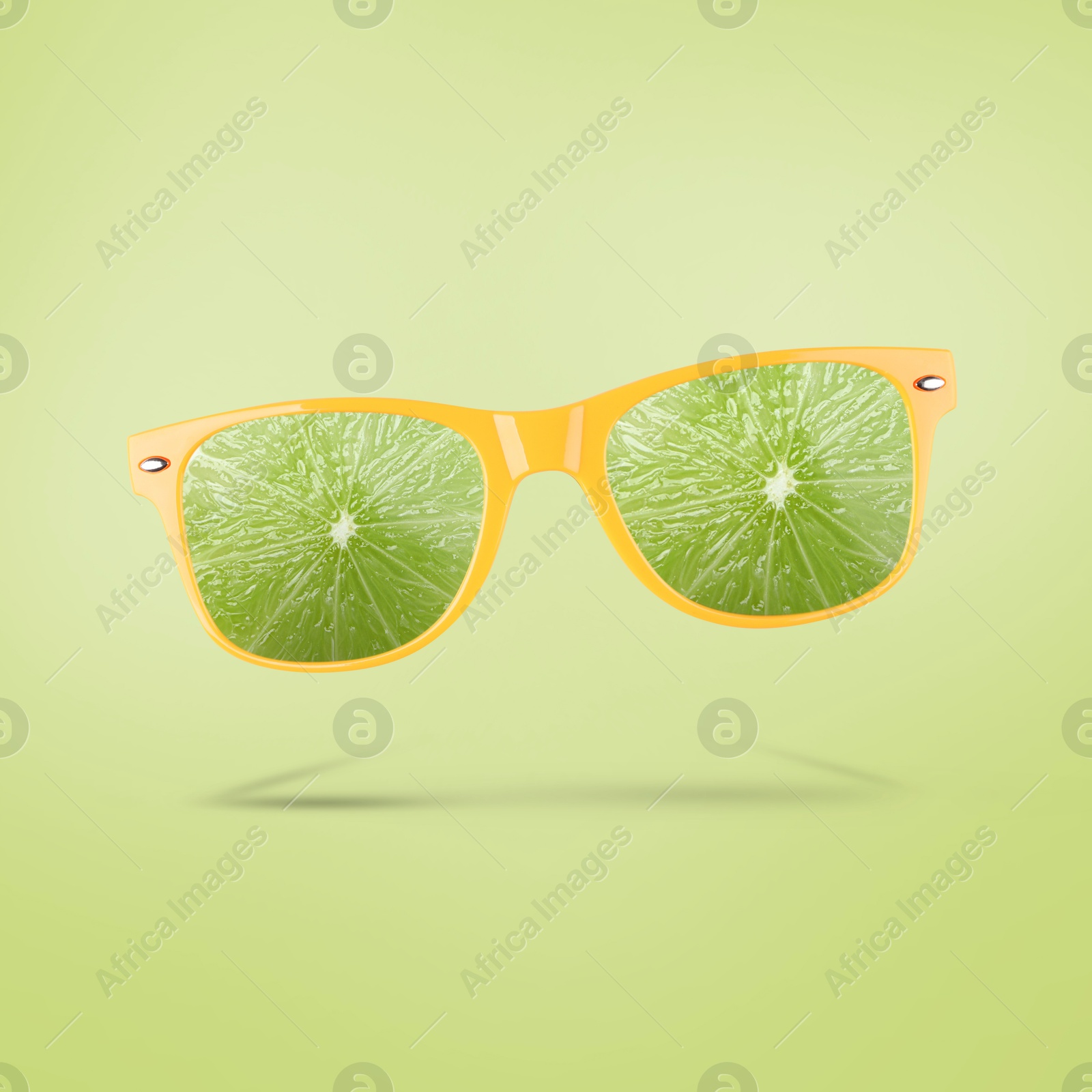 Image of Sunglasses with juicy lime in air on light green background. Summer vibe