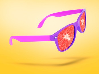 Image of Sunglasses with juicy grapefruit in air on golden background. Summer vibe