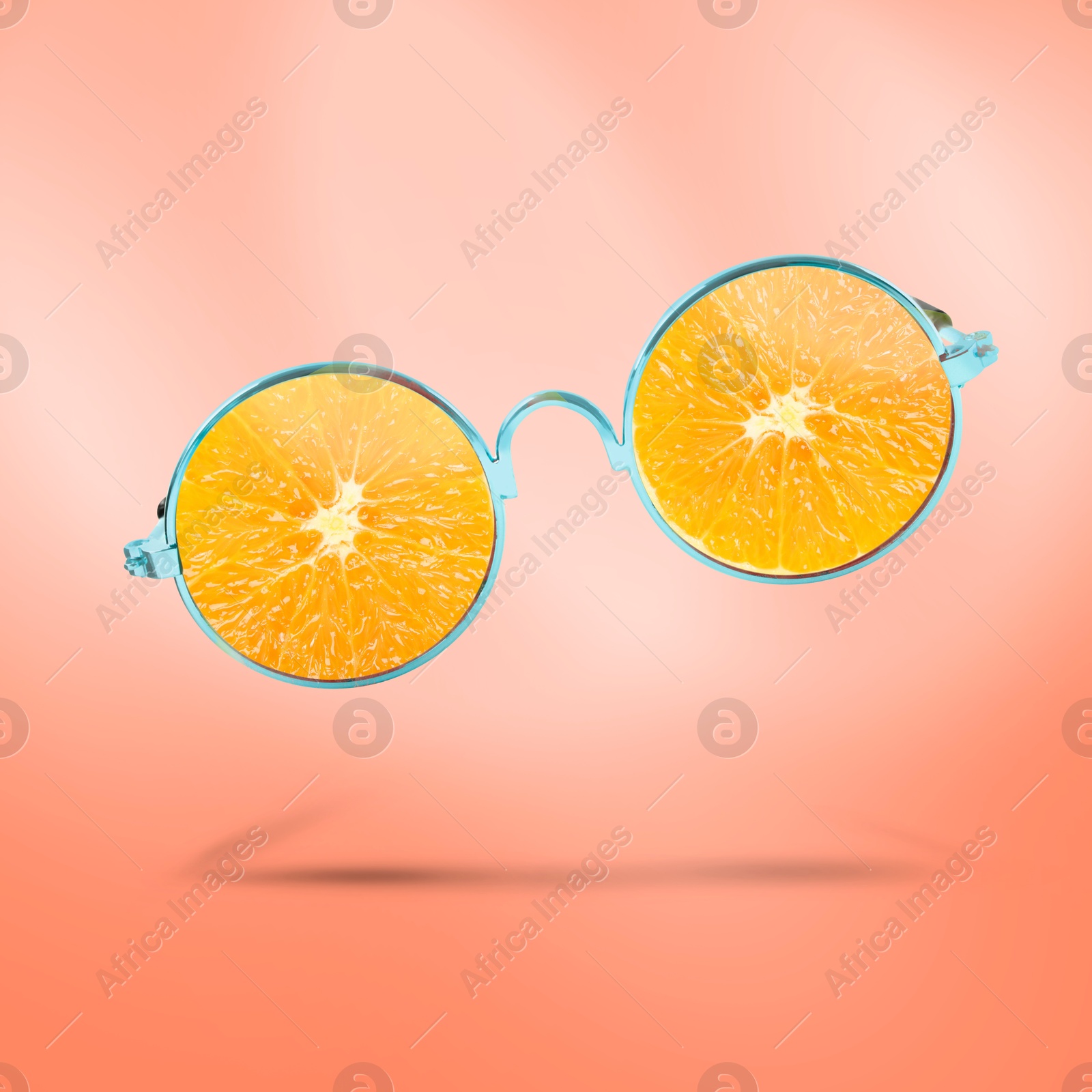 Image of Sunglasses with juicy orange in air on coral background. Summer vibe