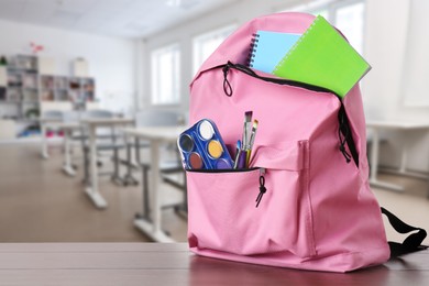 Pink backpack with stationery on school desk in classroom. Space for text