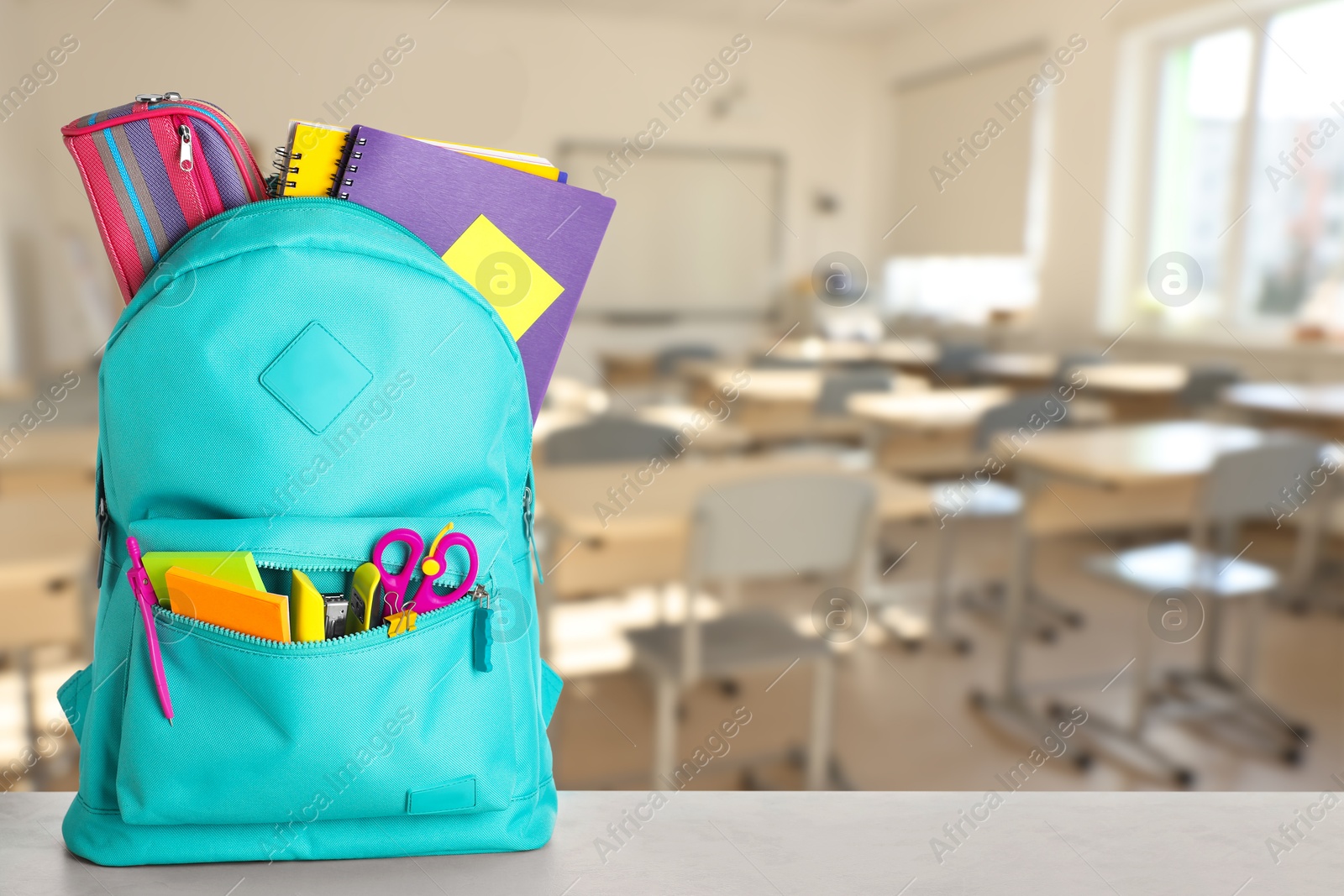 Image of Turquoise backpack with stationery on school desk in classroom. Space for text