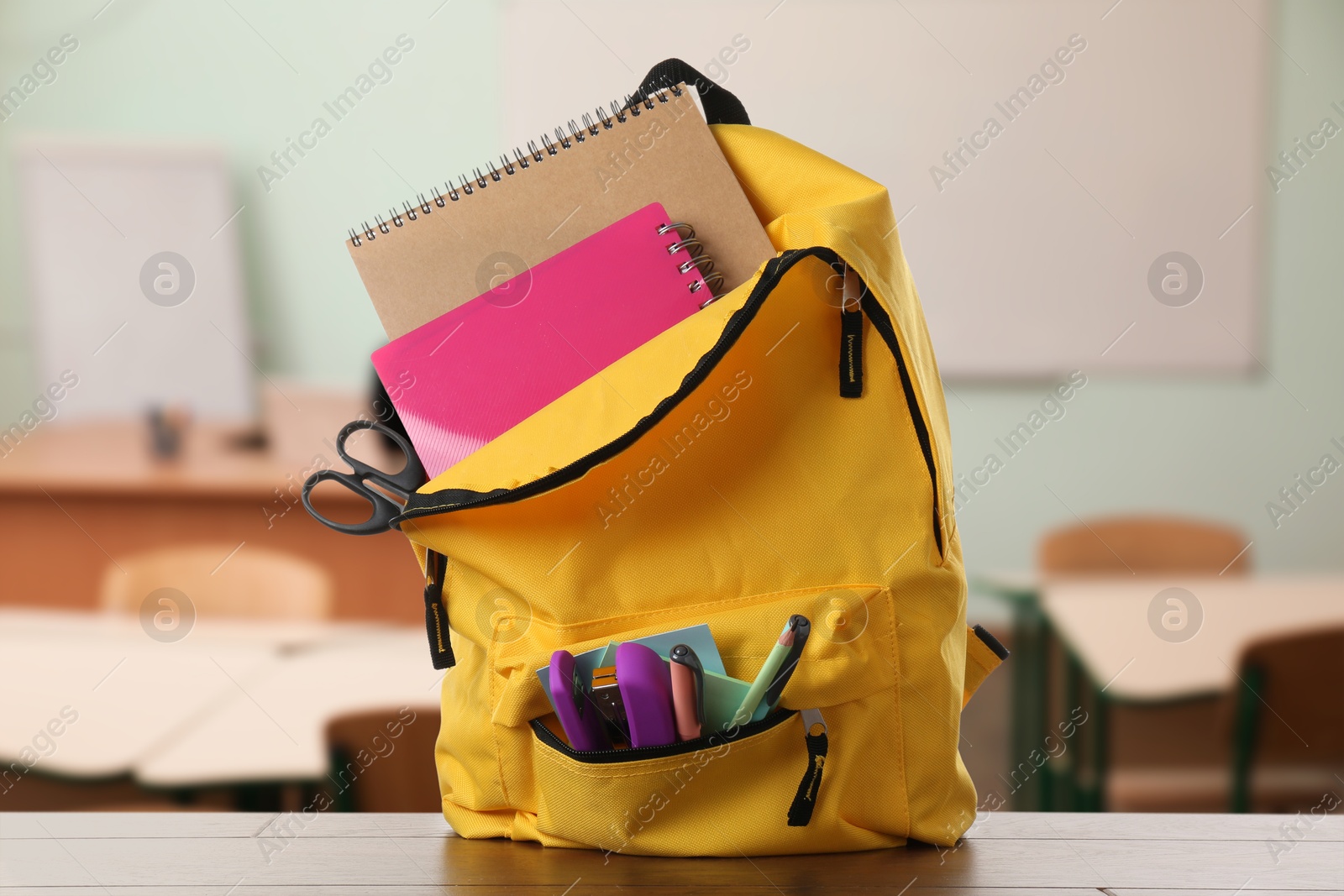 Image of Yellow backpack with stationery on school desk in classroom