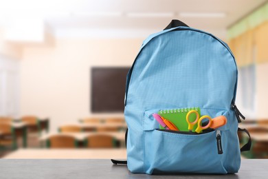 Image of Light blue backpack with stationery on school desk in classroom. Space for text